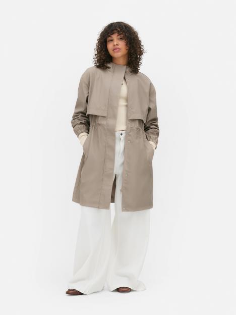 Woman wearing a taupe trench coat and white pants.