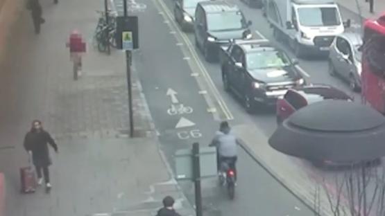 CCTV footage of a man pulling a suitcase, a cyclist, and traffic on a city street.