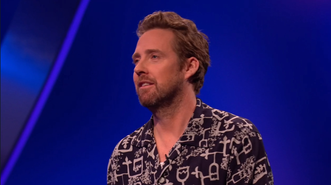 Screenshot of a man speaking in front of a blue background.