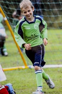 Photo of a young boy in a green soccer uniform running on a field.