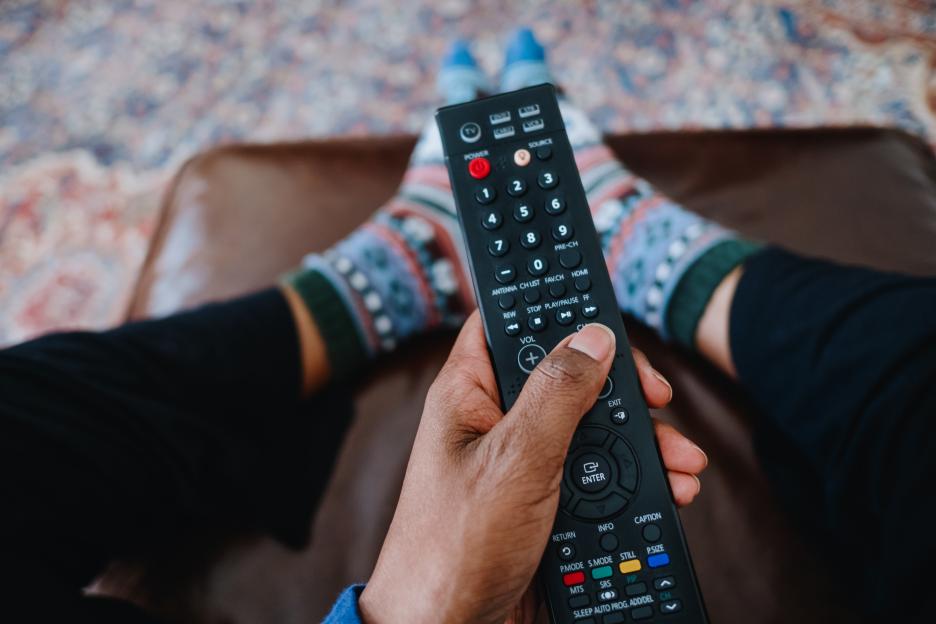 Person relaxing on a couch, holding a TV remote.