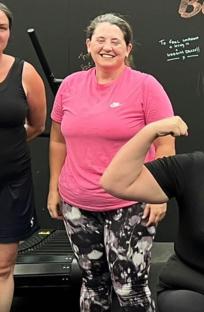 Woman in pink shirt and patterned leggings flexing her bicep.