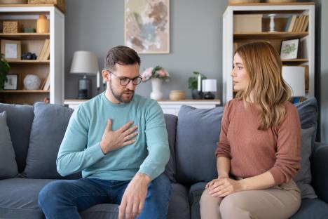 A couple sits on a sofa having a serious conversation.