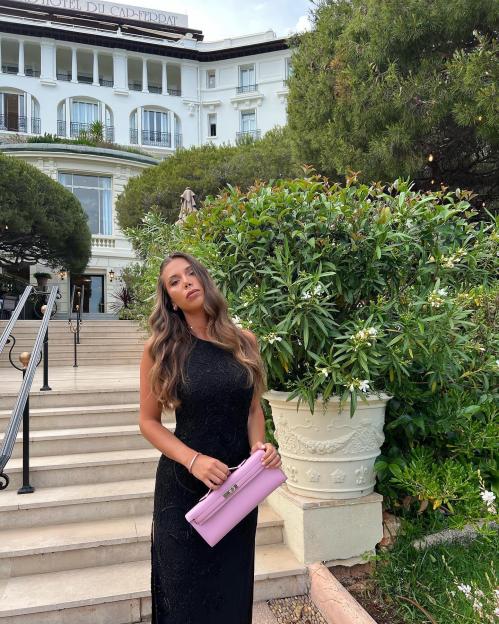 Laura Villars in a black gown holding a pink clutch in front of Hotel du Cap-Ferrat.