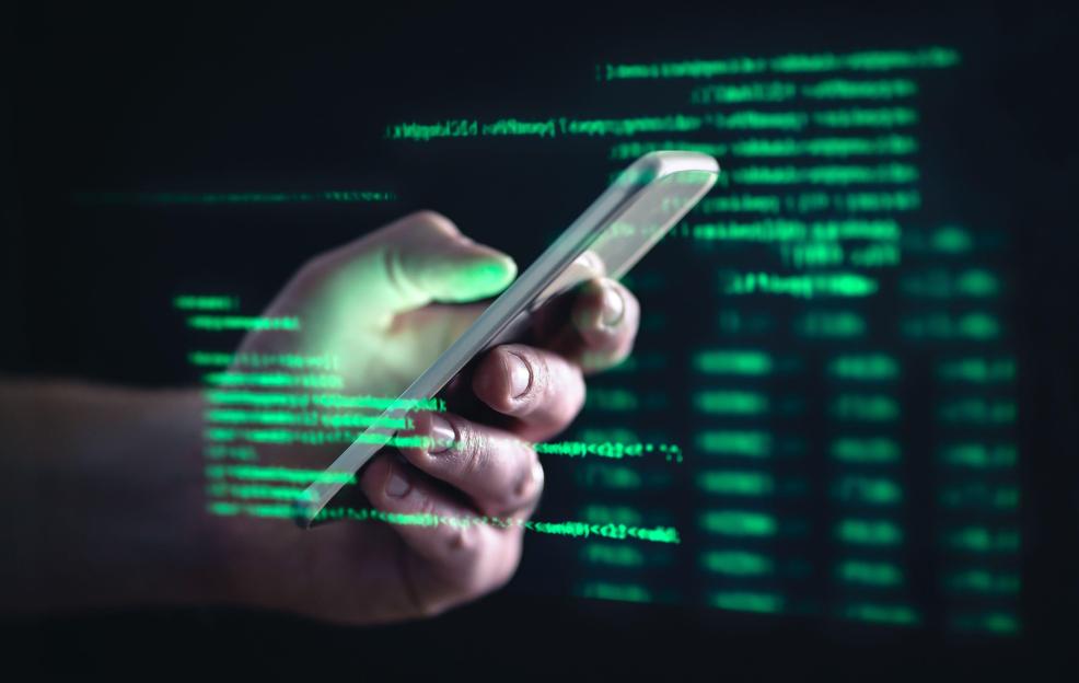 Hand holding smartphone with green code in the background.
