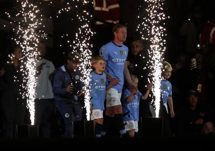 Kevin De Bruyne with children in Manchester City jerseys, surrounded by fireworks.