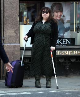 Woman with a cane and suitcase outside a London courthouse.
