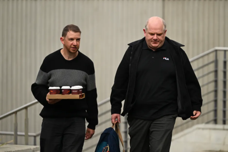 Two men walking, one carrying coffee.