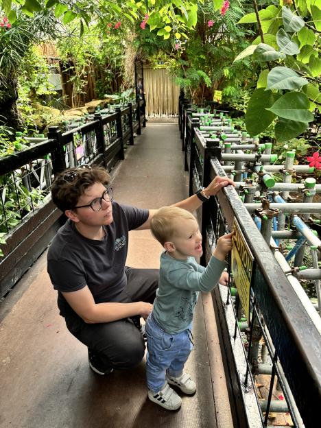 An adult and toddler look at a caution sign in a botanical garden.