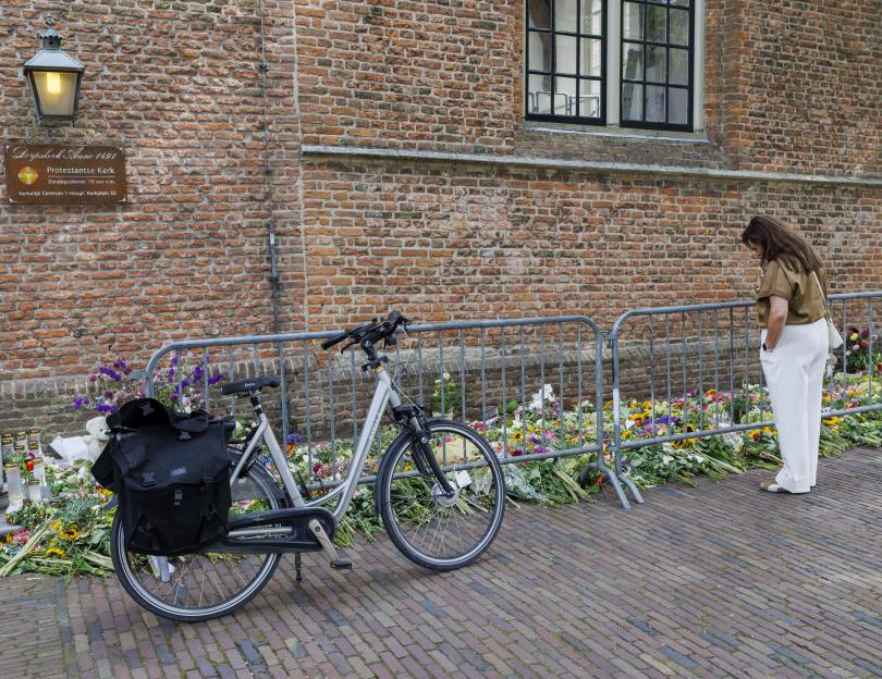 A woman stands by a bike and floral tributes outside a church.