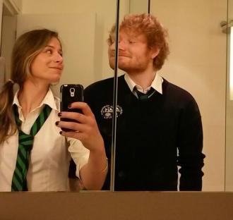 Ed Sheeran and a woman taking a selfie in a mirror, both wearing school uniforms.