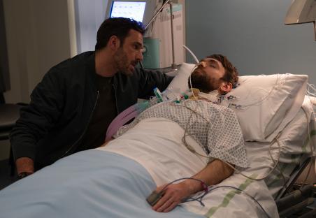 A man visits a man lying in a hospital bed.