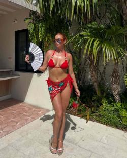 Woman in red bikini and sarong holding a hand fan.