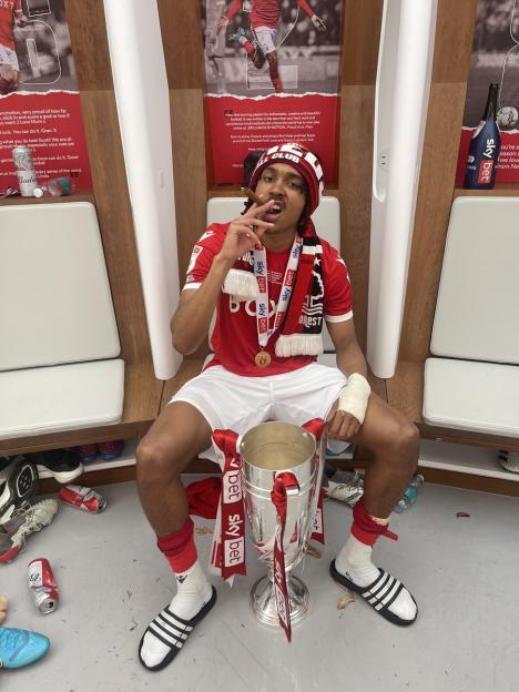 Djed Spence holding a trophy and smoking a cigar in a locker room.