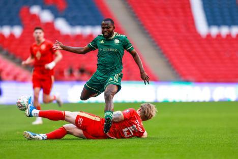 Soccer player in green making a tackle on a player in red.