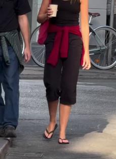 Woman walking down the street wearing black shorts and flip-flops, carrying a coffee cup.