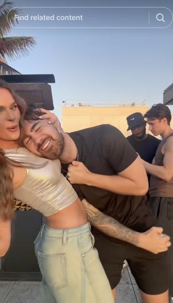 Screenshot of a group of young people on a rooftop; a woman is playfully hugging a man from behind.