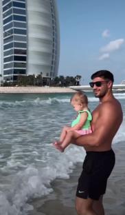 a shirtless man is holding a baby on the beach