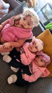 Three babies, one older sister and twin infants, wearing pink clothing and headbands.