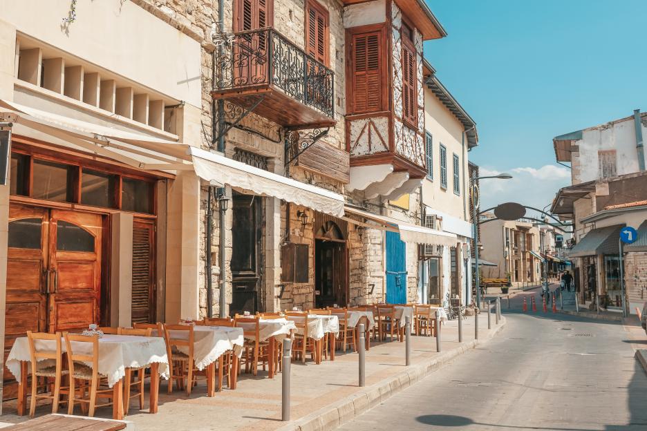 Outdoor cafe tables and chairs line a narrow street in Limassol, Cyprus.