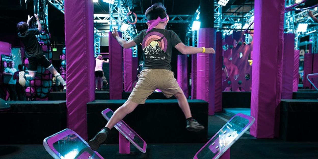 People of various ages engaging in an indoor ninja obstacle course.
