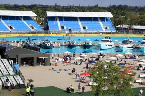 Overview of a Formula 1 Miami Grand Prix fan zone with bleachers, boats in a pool, and people relaxing.