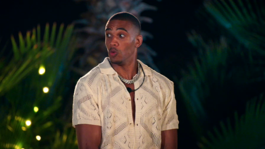 Man with a surprised expression, wearing a cream knit shirt and a thick silver chain.