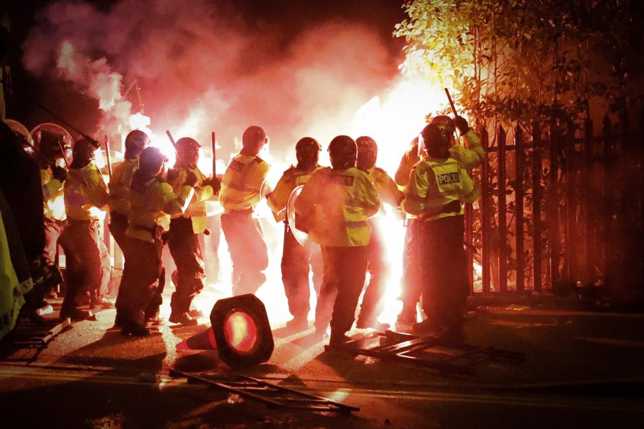 Police clashing with Legia Warszawa fans amidst flares.