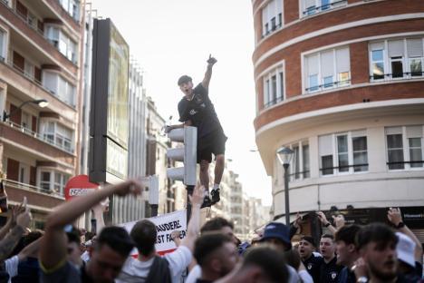 A man standing on a traffic light celebrates amidst a cheering crowd.