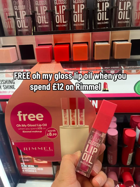 A display of Rimmel "Oh My Gloss! Lip Oil" products in various shades, with a promotional sign offering a free lip oil when spending £12 on Rimmel makeup.