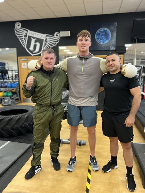 Three men posing in a gym, with boxing gloves on two of them.