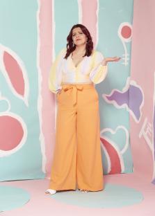 Portrait of Roxanne Hoyle, wearing an orange pantsuit and a pastel top, against a colorful background.
