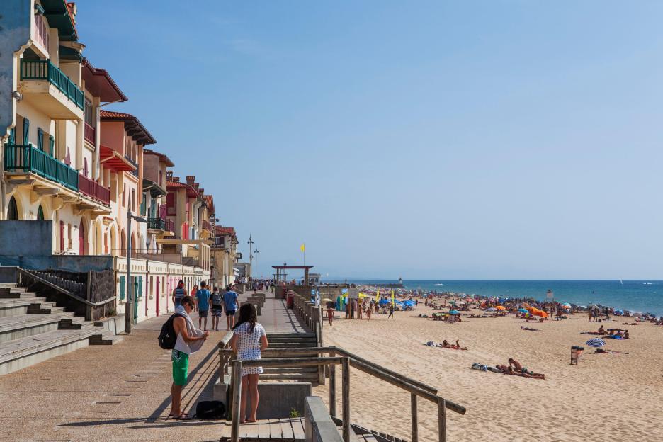 Beachfront boardwalk in Hossegor, France, with people walking and relaxing on the beach.