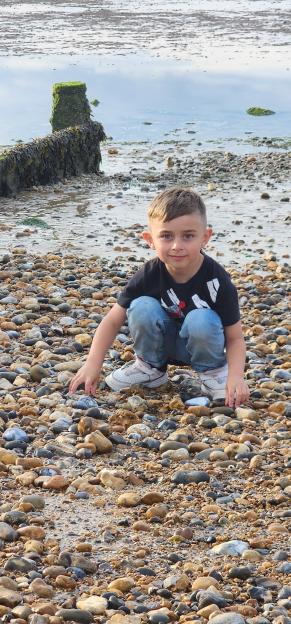 Young boy crouching on a pebble beach.