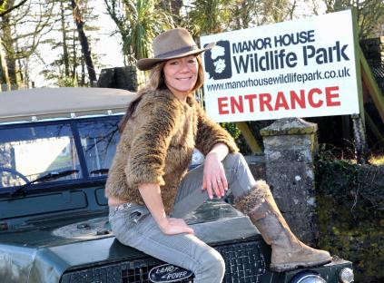 Woman sitting on a Land Rover in front of Manor House Wildlife Park entrance sign.