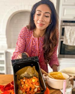 Woman holding an air fryer basket of roasted butternut squash and onions.