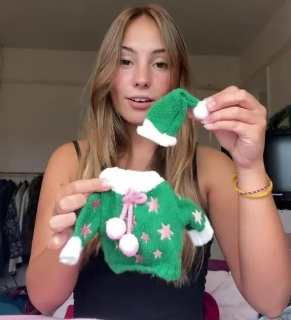 Woman holding up a miniature green sweater with pink stars and a matching hat with a white pom-pom.