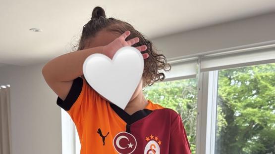 Toddler in Galatasaray jersey covering face with hand.