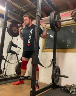 Man squatting with barbell in a power rack.