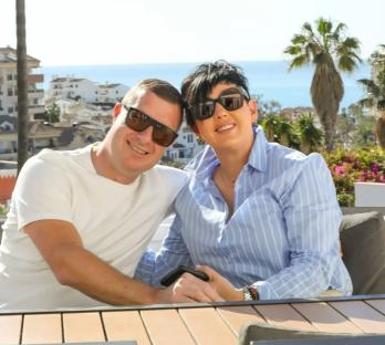 Couple smiling outdoors at a table.