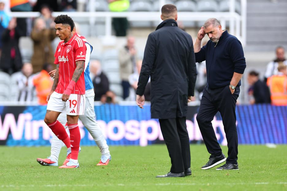 A disheartened Nottingham Forest head coach Ange Postecoglou walks off the field alongside a player in a red jersey.