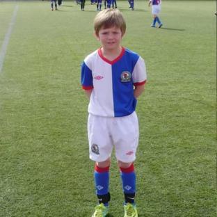 Young boy in Blackburn Rovers soccer uniform on a field.