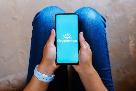 Person holding a smartphone displaying the Skyscanner logo.