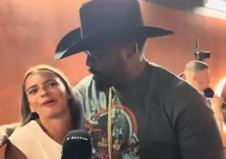 A man in a cowboy hat speaks with a woman in front of a microphone.