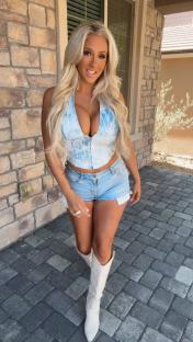 Woman in a light blue top and denim shorts wearing white cowboy boots.