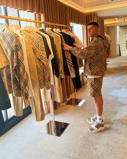 Man in Burberry patterned clothing examining clothes on a rack.