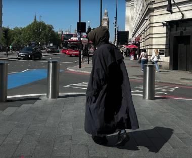 Person in long dark coat walking in London, Big Ben in the background.