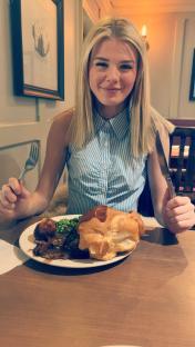 A young woman sits at a table, ready to eat a plate of roast beef dinner.