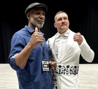Two men at a boxing event; one gives a thumbs up.