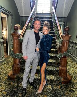 Couple posing on a staircase decorated for the holidays.